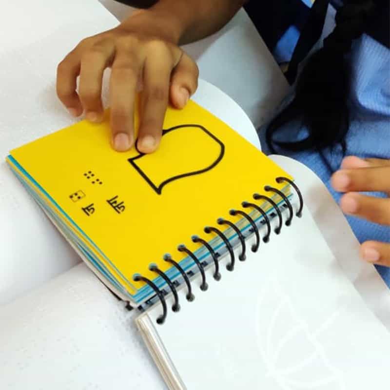 A student reading a page from Braille Hindi Varnamala Aur Ginti tactile picture braille book by Beyond Braille