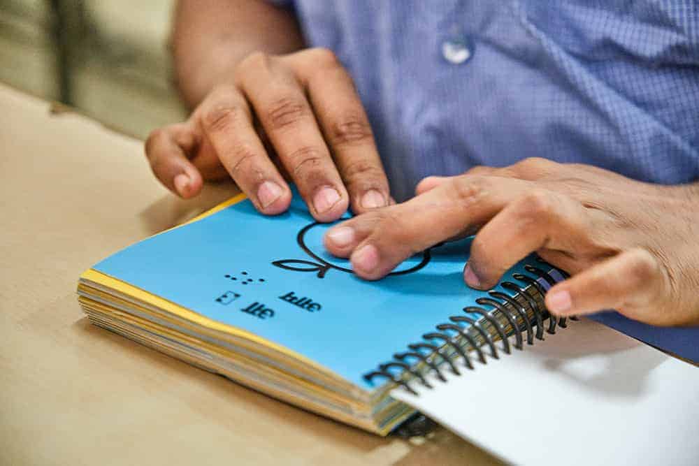 A student sensing a Braille mango photo with his finger tips in beyond Braille book
